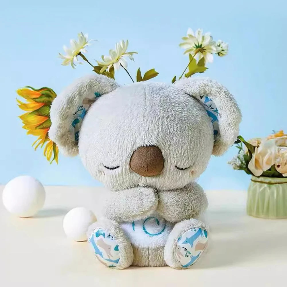 Plush grey koala toy with patterned ears, sitting near flowers on a light blue background