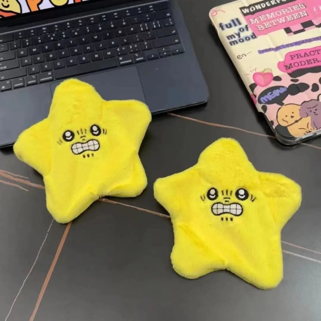 Two plush yellow star toys with cartoon faces on a desk beside a laptop and tablet.